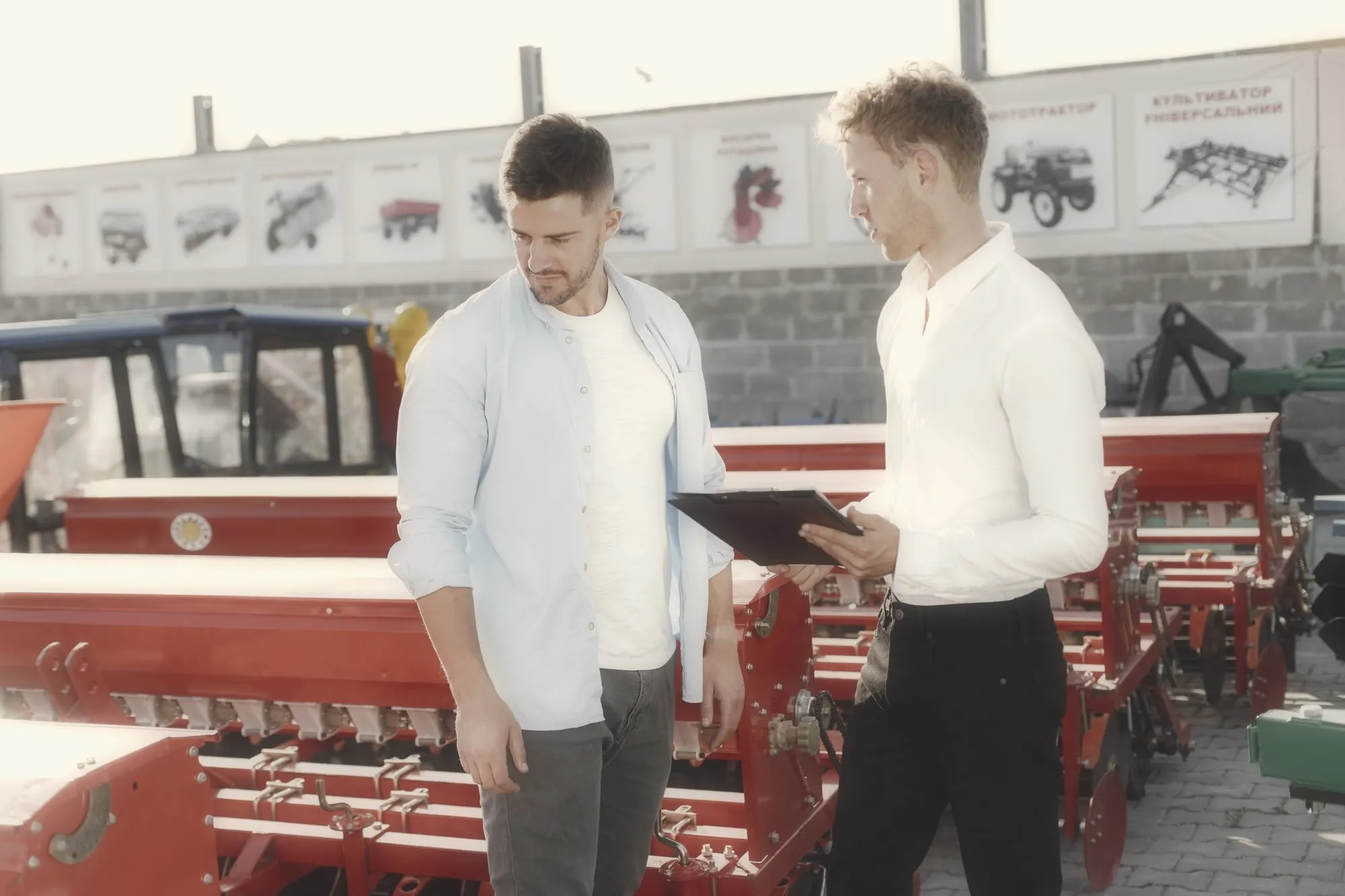 A sales rep and a customer talking beside a row of farm machinery in a dealer yard