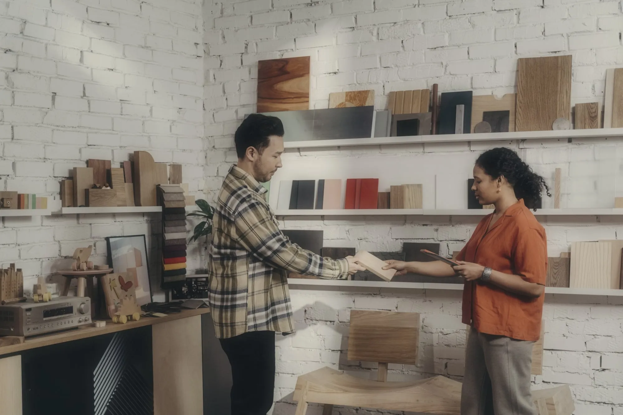 A consultant hands a wood sample to a client in a showroom with shelves of wood and colour samples